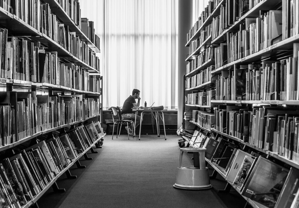 Pasillo de una librería con hombre de fondo leyendo un libro con su ordenador